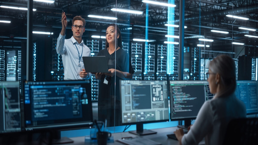 Female e-Business Entrepreneur and Male IT Specialist Discussing Something and Use Laptop in Big Data Center Server Room. Work on Web Services Cloud Computing SAAS Concept